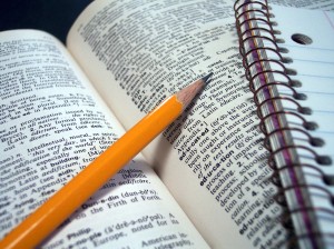 Pencil and notebook lying across dictionary